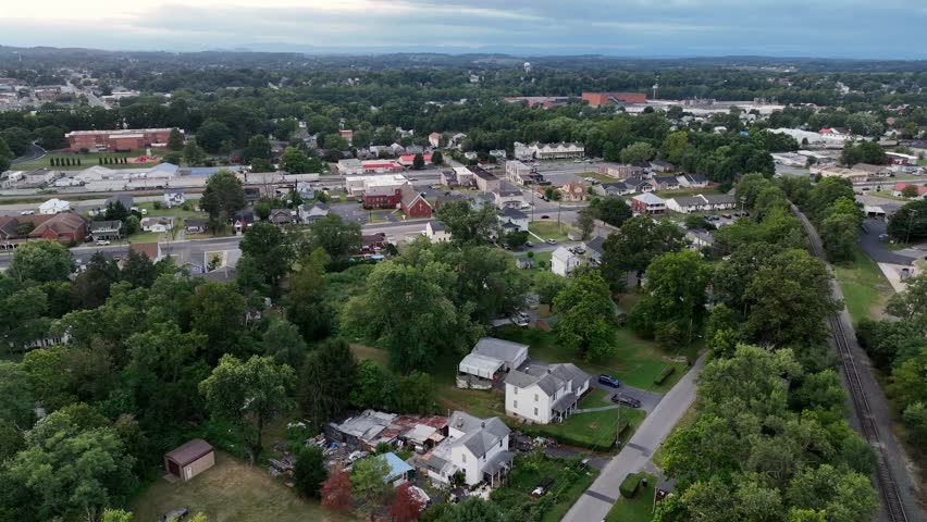 Aerial orbit shot of America. Suburb neighborhood with houses near railway tracks. Green forest trees and red brick school campus in background. Cloudy sunset in town of Virginia, USA. Wide shot.