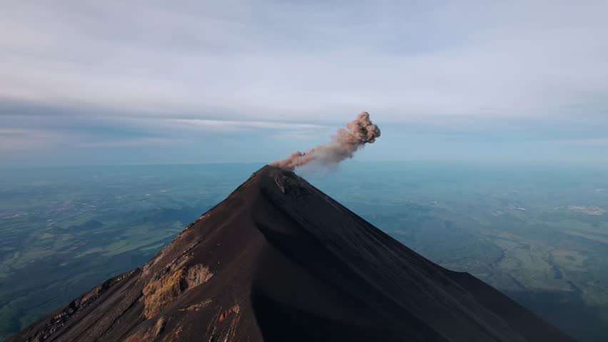 A breathtaking drone shot captures the active Volcán de Fuego in Guatemala, with a plume of ash and gas rising from its summit.