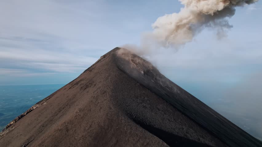 A breathtaking drone shot captures the active Volcán de Fuego in Guatemala, with a plume of ash and gas rising from its summit.