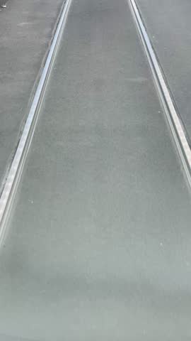 A close-up view of tram tracks on an urban street, highlighting the asphalt texture and the surrounding environment.