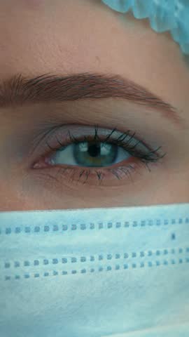 Female in medical blue cap and protective face mask, close up of face. Woman face in medical mask and cap for virus infection prevention and protection. Vertical video