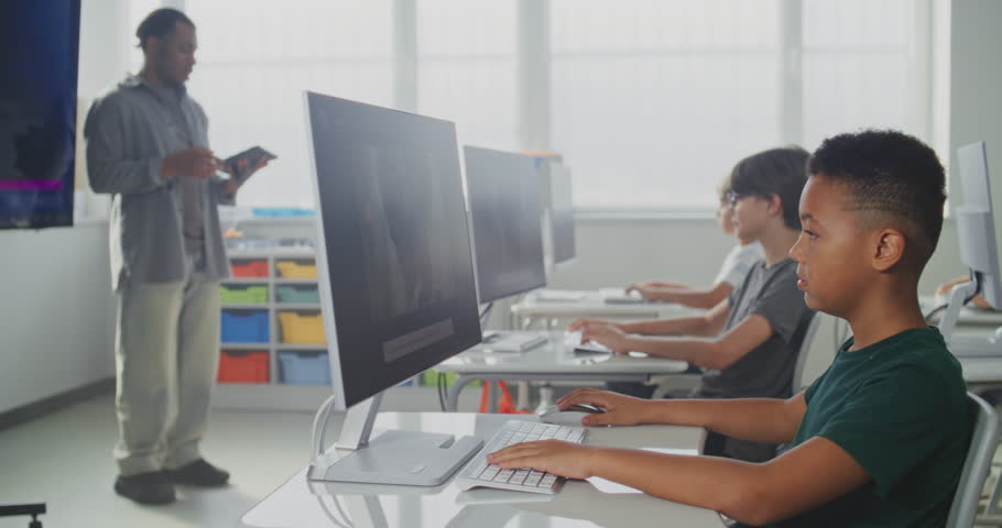 Elementary School Children Using Computers, Creating Illustrations in AI Image Generator. African American Teacher Teaching Young Boys and Girls During Digital Art Lesson. STEM Education. Dolly Shot.