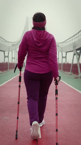 Back side follow view of young fat female doing walking exercises with nordic walking poles in foggy winter morning. Cardio training concept. Vertical video