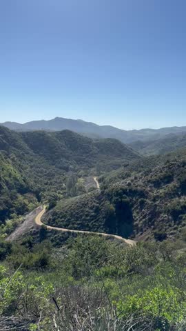 Vertical video of scenic California mountains with a winding road and lush green hills near Los Angeles under a clear blue sky perfect for travel and nature themes.