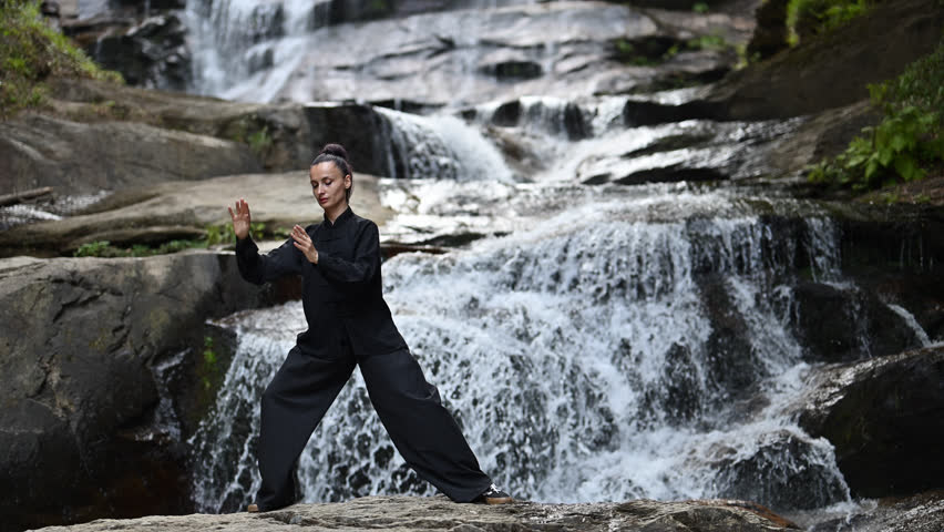 woman performing slow tai chi movements near a waterfall and river at sunset capturing harmony balance and fitness in nature