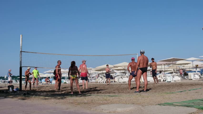 June 28, 2025, Antalya, Turkey. A lively group enjoys a competitive game of beach volleyball during the sunny afternoon at a coastal resort with umbrellas.