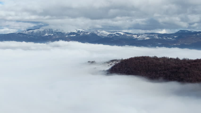 A view of mountains with clouds above the fog in the valley Trees are surrounded by a sea of white clouds Mountain peaks visible in the distance
