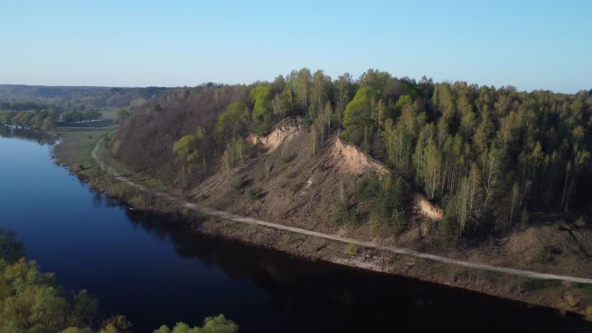Spring landscape: hill by the river. An aerial view of a spring landscape showing a hill covered with trees, a river, and a road