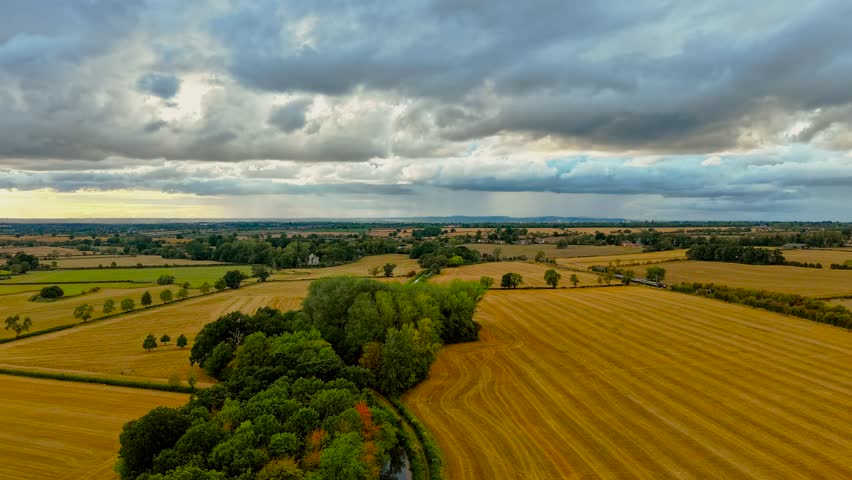 Timelapse storm clouds moving over yellow harvested fields. Countryside horizon stretching with trees along canal. Agricultural farmland under dramatic sky. Rural landscape with storm atmosphere