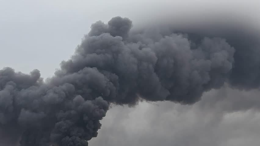 Thick black smoke rising into the sky from an unknown fire or explosion. Could indicate wildfire, industrial accident, or large-scale burning. Concept of danger, pollution, and disaster.