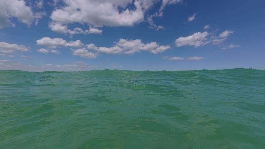 POV view floating in open sea, calm green waves under bright blue sky with scattered clouds, peaceful summer seascape