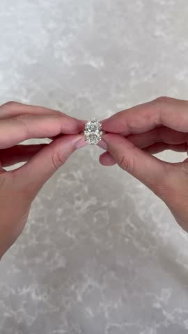 Vertical video featuring close female hand adjusting platinum oval diamond engagement ring or wedding band on gray marble background highlighting sparkle and luxury bridal fashion.