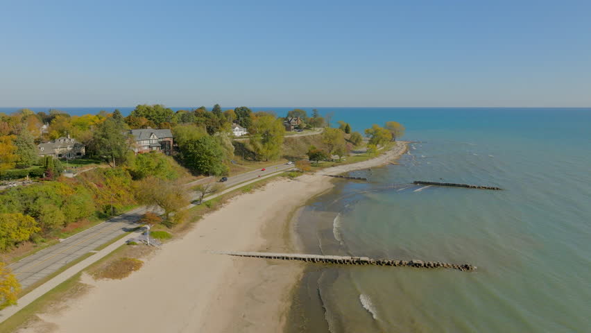 Drone aerial in Sheboygan, Wisconsin with a slow push from Lake Michigan toward the shoreline, neighborhood houses, and colorful autumn trees on a clear fall day.