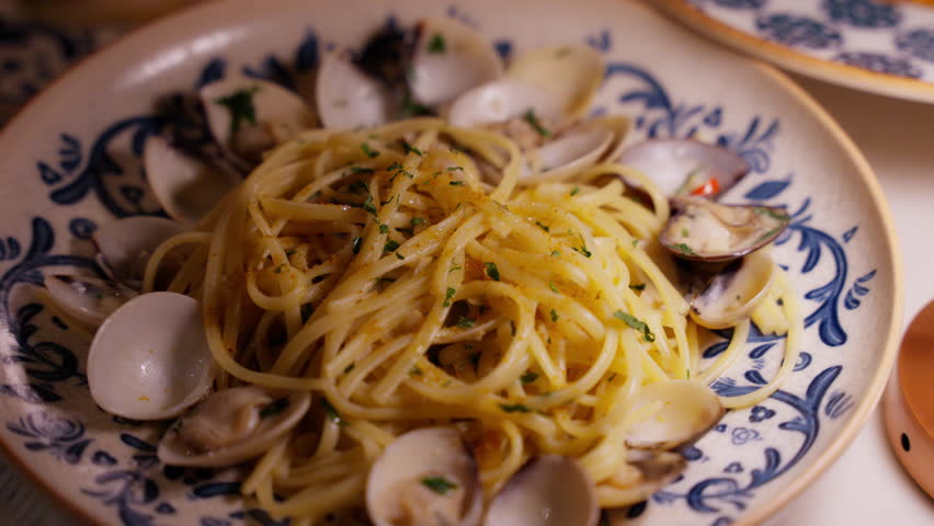 Close-up of vongole pasta served in a stylish white and blue ceramic plate, featuring fresh clams, garlic, and parsley. The elegant presentation and vibrant ingredients make it for culinary videos