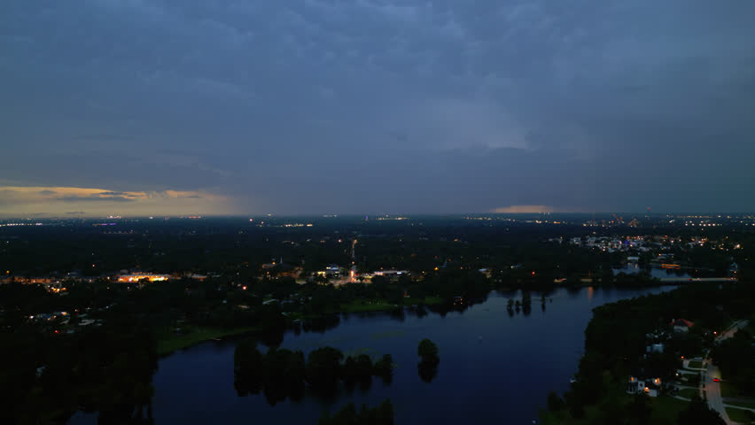 Twilight aerial over darkening water and city skyline, soft ambient light remains, dolly to street lights at dusk