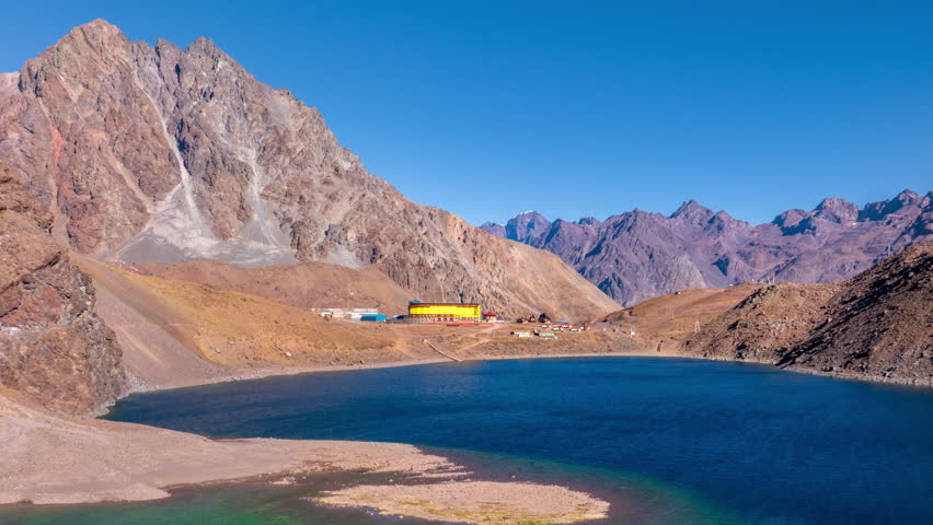 Zoom in hyperlapse approaching Andean lake with blue water and colorful buildings surrounded by mountains in Chile.