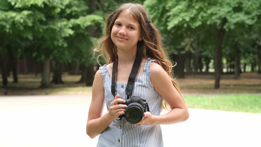 Portrait of kid girl photographer in city park. Child learning to take photos. Young person making images with professional camera