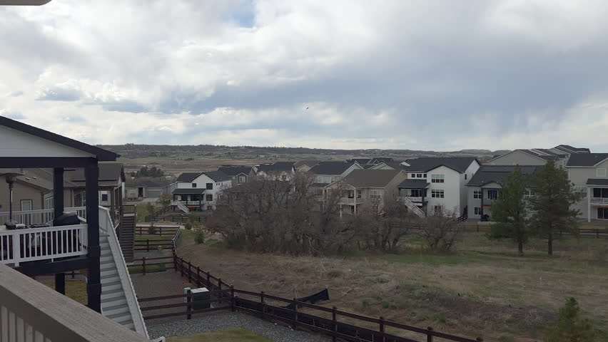 A wide landscape view captures several suburban houses behind a grassy open field lined with trees. The scene is calm and overcast, showing peaceful residential surroundings.