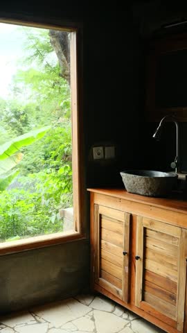 A rustic bathroom with a natural stone sink ,wooden cabinet, with a View of the Jungle through a wide window