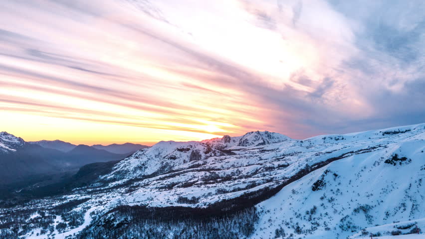 Aerial hyperlapse capturing a stunning sunset over the snowy Andes mountains in Chile, with dramatic skies and vibrant colors.