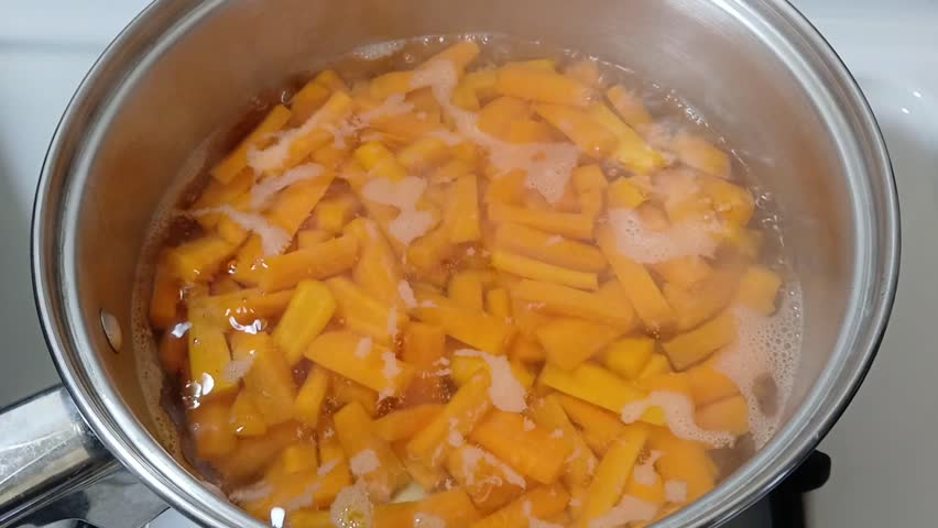 Footage of chopped carrots being cooked in a casserole. The boiling movement and the forming of steam smoke are being captured.