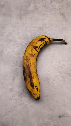 Ripe banana is being lifted from a textured surface, showcasing the gradual action of picking it up, highlighting its vibrant color and details