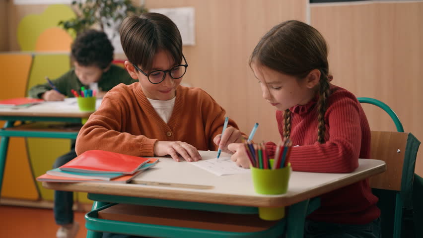 Three diversity children in school classroom two Caucasian classmates boy with girl writing drawing together African American kid child walking look at picture asking talking go away study education
