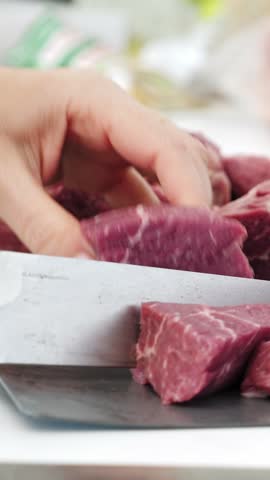 Woman cutting uncooked beef on pieces for barbecue. Prepare meat for bbq. Closeup. Vertical footage