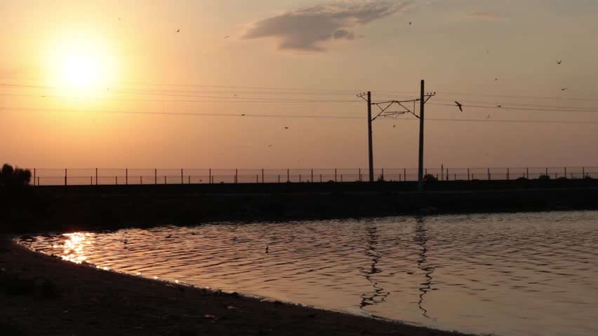 Railway track at sunset beside serene lake, golden-hour landscape with tranquil water and warm light.