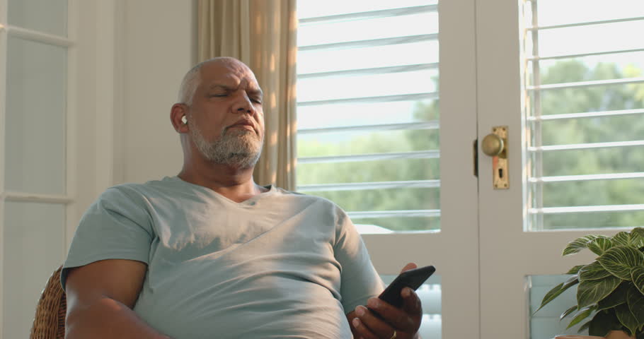 Senior man relaxing at home, listening to music on smartphone with earbuds. Technology, lifestyle, leisure, headphones, wireless, relaxation