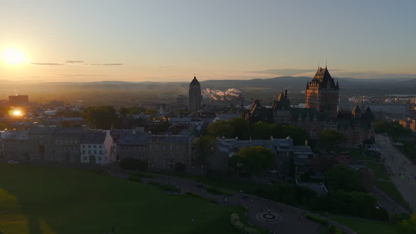 Aerial view of Quebec City at sunset with the Canadian flag waving above historic architecture. Warm golden light over Old Quebec with Château Frontenac in the background. Perfect for travel, tourism, culture, heritage, and national identity concepts.