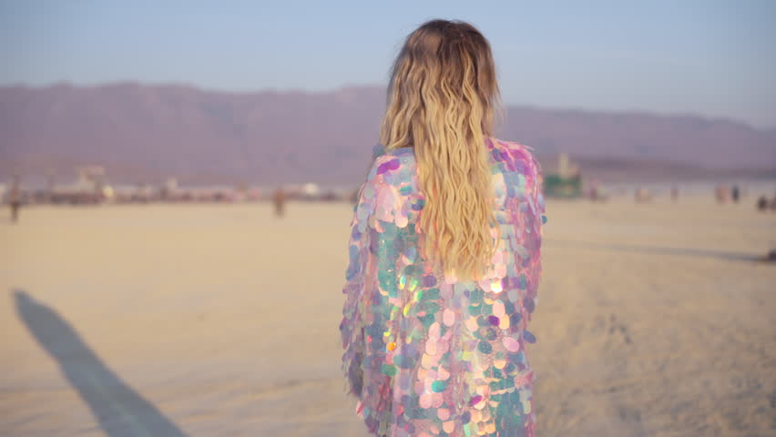 Woman in futuristic sequin outfit with wide hat posing at desert music and art festival in USA. Alternative fashion, freedom, creative atmosphere and unique celebration under sunlight