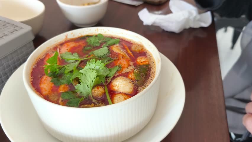 A bowl of authentic Tom Yum soup, a spicy and sour Thai dish, being stirred with a spoon. Ideal for showcasing Asian food, cooking, or healthy eating.