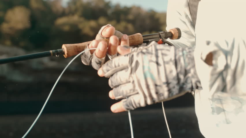 Extreme slow motion closeup of fly fisherman’s gloved hand pulling fishing line through fingers, droplets falling as line tightens during river angling