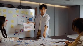 Young businessman conference speaker passionately explains business project strategy using a whiteboard, engaging a diverse team in collaborative brainstorming within a contemporary office environment - Powered by Shutterstock - Get 15% off with code: PIKWIZARD15