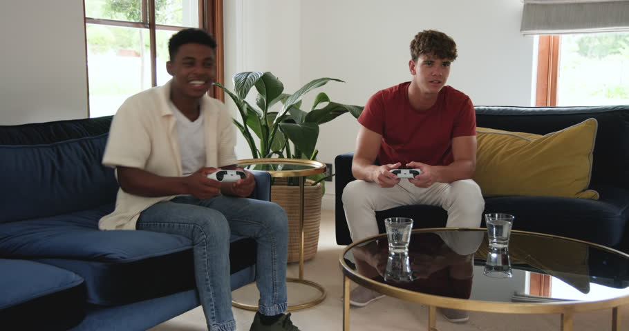 Diverse male friends playing with controllers on sofa reacting to challenge consoling after loss. Gaming, friendship, casual, modern, entertainment, competitive, relaxation