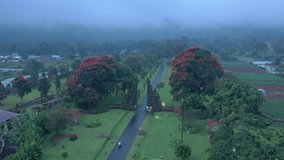 Traditional Balinese split stone gates rising against a lush garden with green lawns, tropical trees, and vibrant red flowers, surrounded by mystical morning mist - Powered by Shutterstock - Get 15% off with code: PIKWIZARD15
