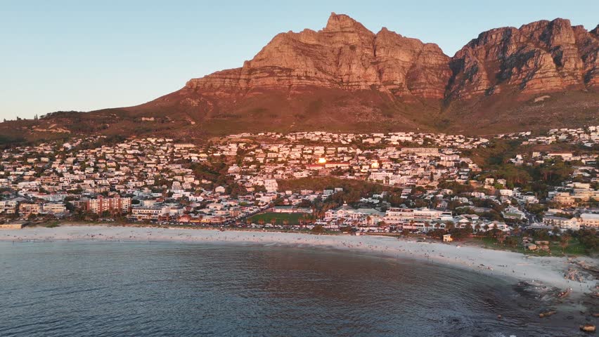 High angle drone footage approaching Lion’s Head and Atlantic coastline at sunset in Camps Bay beach with dramatic lighting at sunset , Cape Town South Africa
