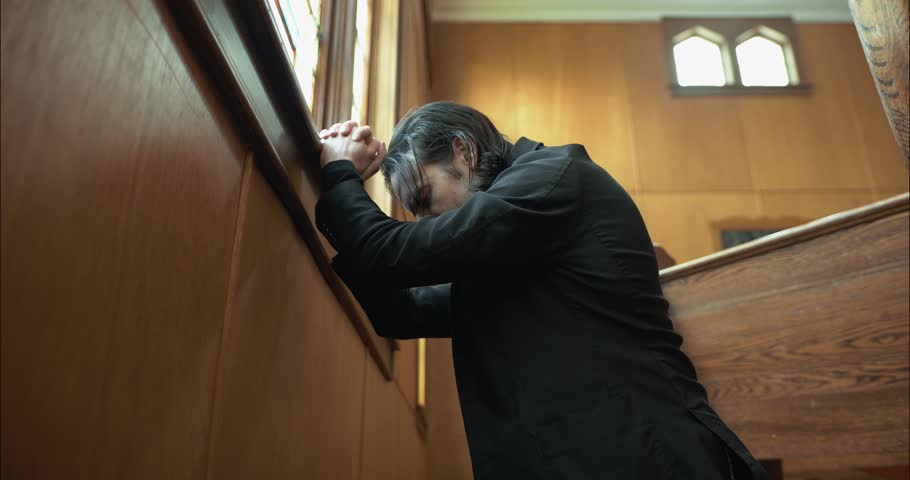 A Christian man, priest, preacher, pastor praying on his knees inside an old church.