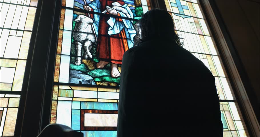 Man in silhouette looking at stained-glass art inside a church sanctuary, conveying a cinematic, moody, and contemplative atmosphere.