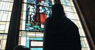 Man in silhouette looking at stained-glass art inside a church sanctuary, conveying a cinematic, moody, and contemplative atmosphere. - Powered by Shutterstock - Get 15% off with code: PIKWIZARD15