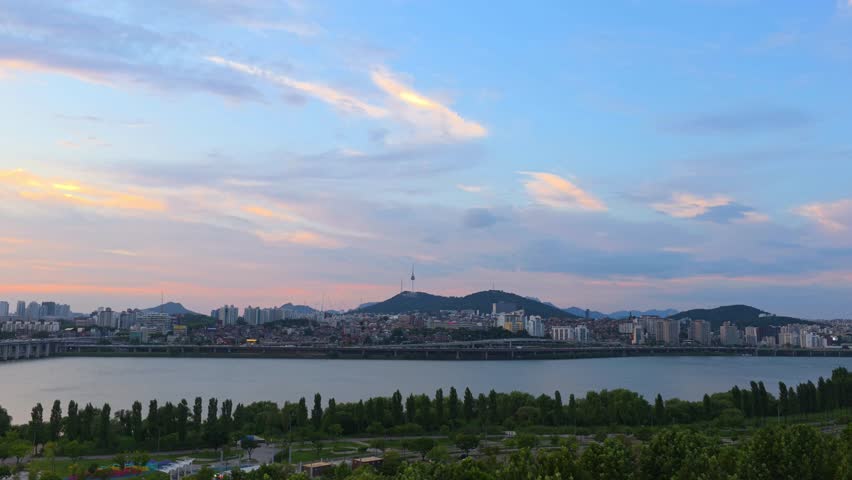 Aerial view of Seoul cityscape at sunset featuring Namsan Tower, Yongsan District, and Hangang River park with colorful evening clouds.