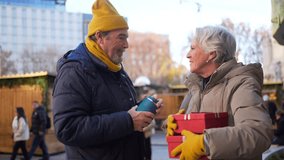 Loving senior couple sharing heartwarming moment while exchanging festive gifts amid twinkling christmas market decorations and winter atmosphere - Powered by Shutterstock - Get 15% off with code: PIKWIZARD15