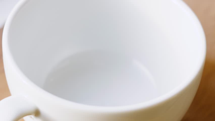 Fresh Morning Coffee Being Poured into White China Mug in Slow Motion with Bubbles on Top After Pouring is Finished.