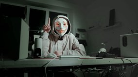 Hooded anonymous hacker in scary mask working at computer in dark environment. Concept of cybercrime, data breach and importance of online protection. - Powered by Shutterstock - Get 15% off with code: PIKWIZARD15