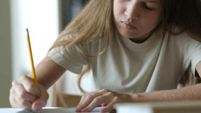 Young girl write in textbook with pencil sitting at table close up. Child doing homework, studying at home. Education and school tasks concept - Powered by Shutterstock - Get 15% off with code: PIKWIZARD15