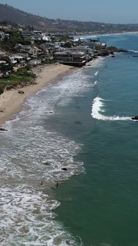 Aerial view of ocean waves crashing onto a sandy beach with homes nestled on the coastline, Malibu, Ca, United States.