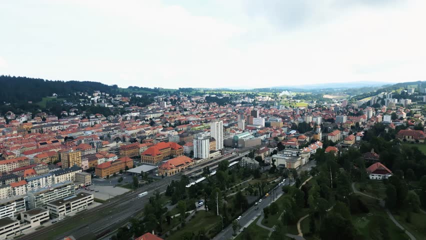 Aerial view of the city showcasing buildings with red rooftops and green trees, contrasting with the grey and white structures, La Chaux-de-Fonds, Neuchâtel, Switzerland.