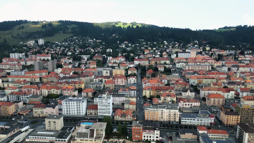 Aerial view of the town, showcasing the architectural layout with red-tiled roofs contrasting against the green hills, La Chaux-de-Fonds, Neuchâtel, Switzerland.