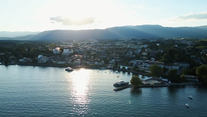 Aerial view of Lake Geneva shoreline at dusk, where the sun reflects off the water towards the town, Lake Geneva, Nyon, Switzerland.
